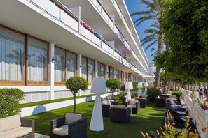 A hotel with a long corridor, outdoor seating area, and a pool. - Arenal (Sant Antoni de Portmany)