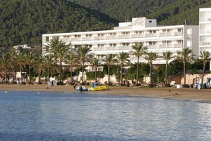 Un hotel de varios pisos, una playa en primer plano y palmeras.