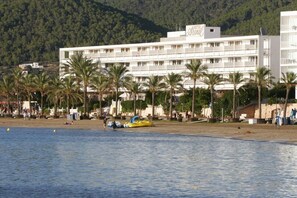 Un hotel con diversi piani, una spiaggia in primo piano e palme.