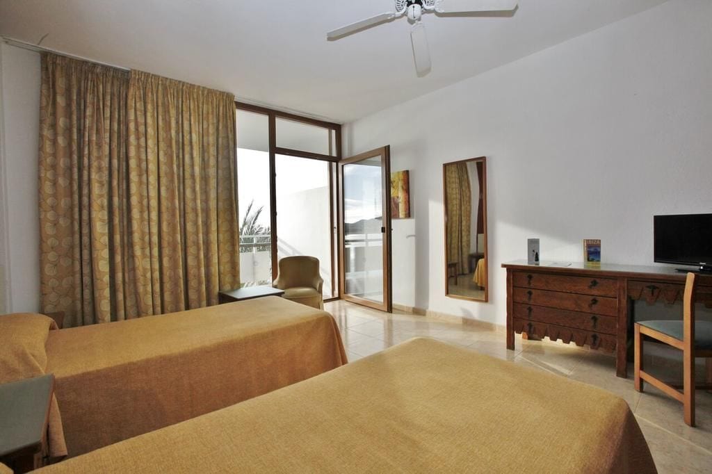 A hotel room with two beds, a desk, a chair, a television, and a large window with curtains.