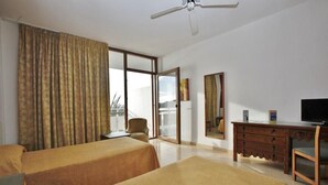 Ein Hotelzimmer mit zwei Betten, einem Schreibtisch, einem Sessel, einem Fernseher und einem großen Fenster mit Vorhängen.