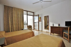 A hotel room with two beds, a desk, a chair, a television, and a large window with curtains. - Arenal (Sant Antoni de Portmany)