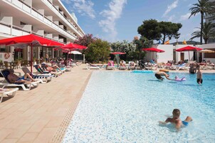 Un área de piscina con sillones de descanso y sombrillas, piscina e edificio con balcones.