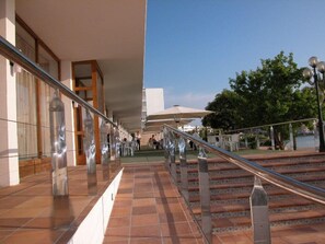 A corridor with a tiled floor, metal railings, and a view of a body of water. - Arenal (Sant Antoni de Portmany)