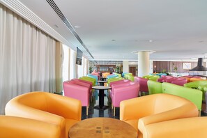 Un vest íbulo de hotel con asientos coloridos, una mesa central y vistas al comedor.