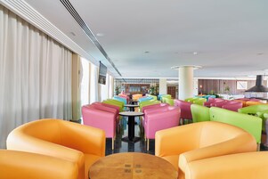 Un vestíbulo de hotel con asientos coloridos, una mesa central y vistas al comedor.