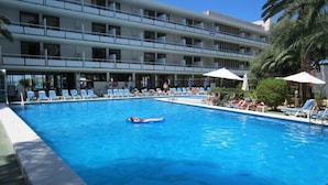 A swimming pool with lounge chairs and umbrellas, surrounded by a multi-story building with balconies. - Arenal (Sant Antoni de Portmany)