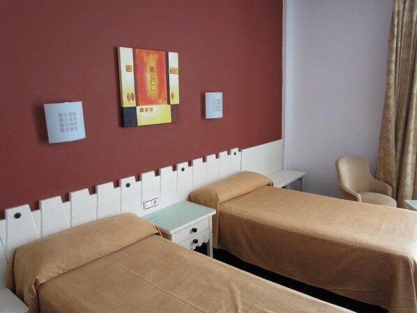 A hotel room with two beds, a white headboard, a small bedside table, a chair, and a wall-mounted thermostat. - Arenal (Sant Antoni de Portmany)