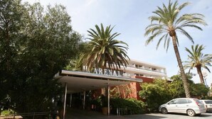A hotel with a covered entrance, palm trees, and a clear sky. - Arenal (Sant Antoni de Portmany)