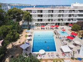 Un hotel con piscina rodeada de tumbonas y sombrillas, con vistas a un puerto deportivo.