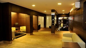 Un moderno hall de hotel con suelo de madera, una zona de estar con sofá y sillas, y un mostrador de recepción.