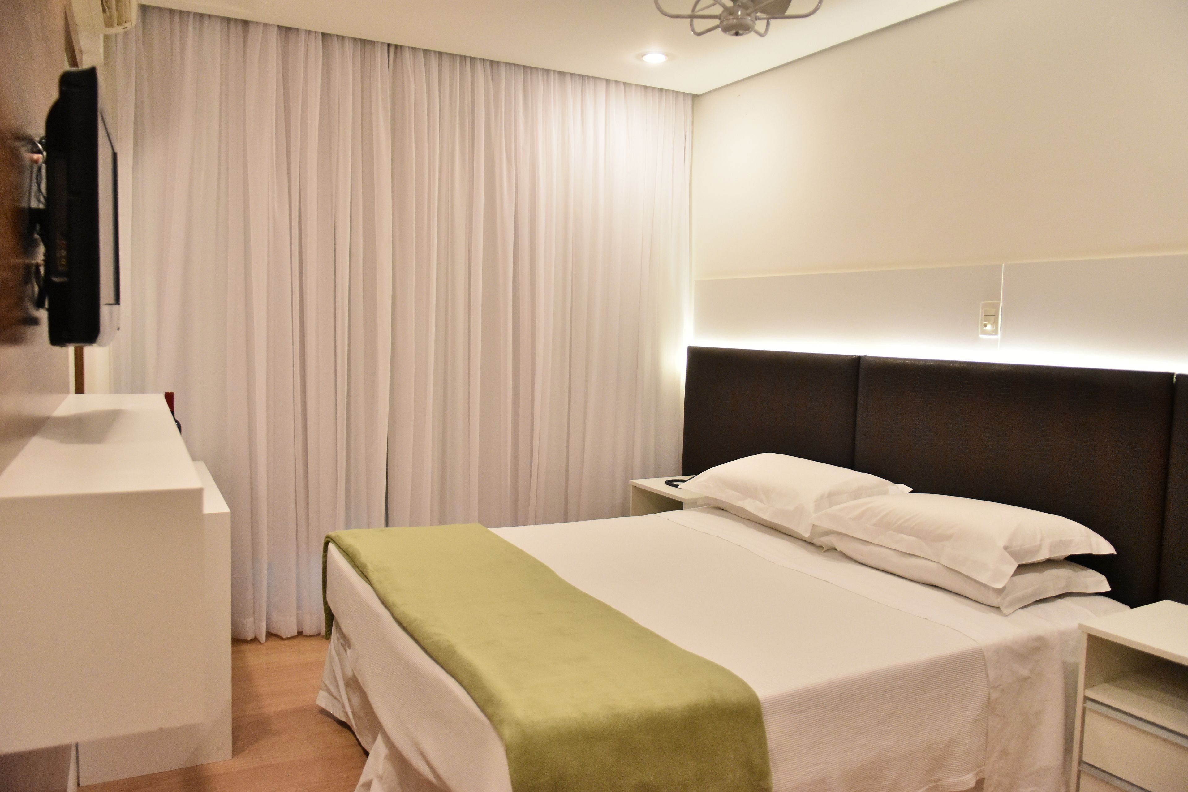 A hotel room with a bed, a bedside table, a desk, and a chair.