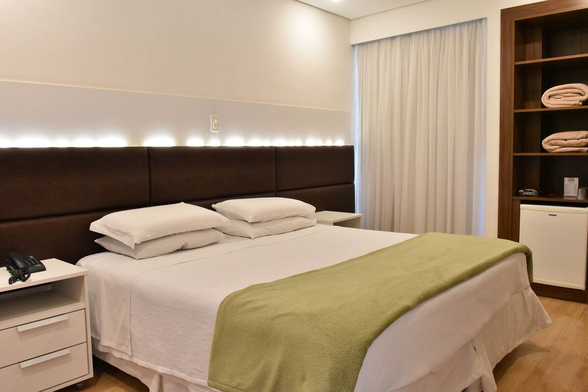 Ein ordentlich bezogenes Bett mit grüner Decke, einem Nachttischtelefon und einem kleinen Nachttisch mit Schubladen.