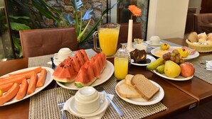 Una mesa de desayuno con platos de comida, una jarra de jugo de naranja y un florero con una flor.