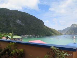 A coastal view with boats, a mountain, and a building with a green roof.