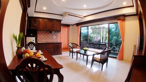 A dining area with a wooden table and chairs, a kitchen with wooden cabinets, and a large window with curtains. - Golden Villa (Pattaya)