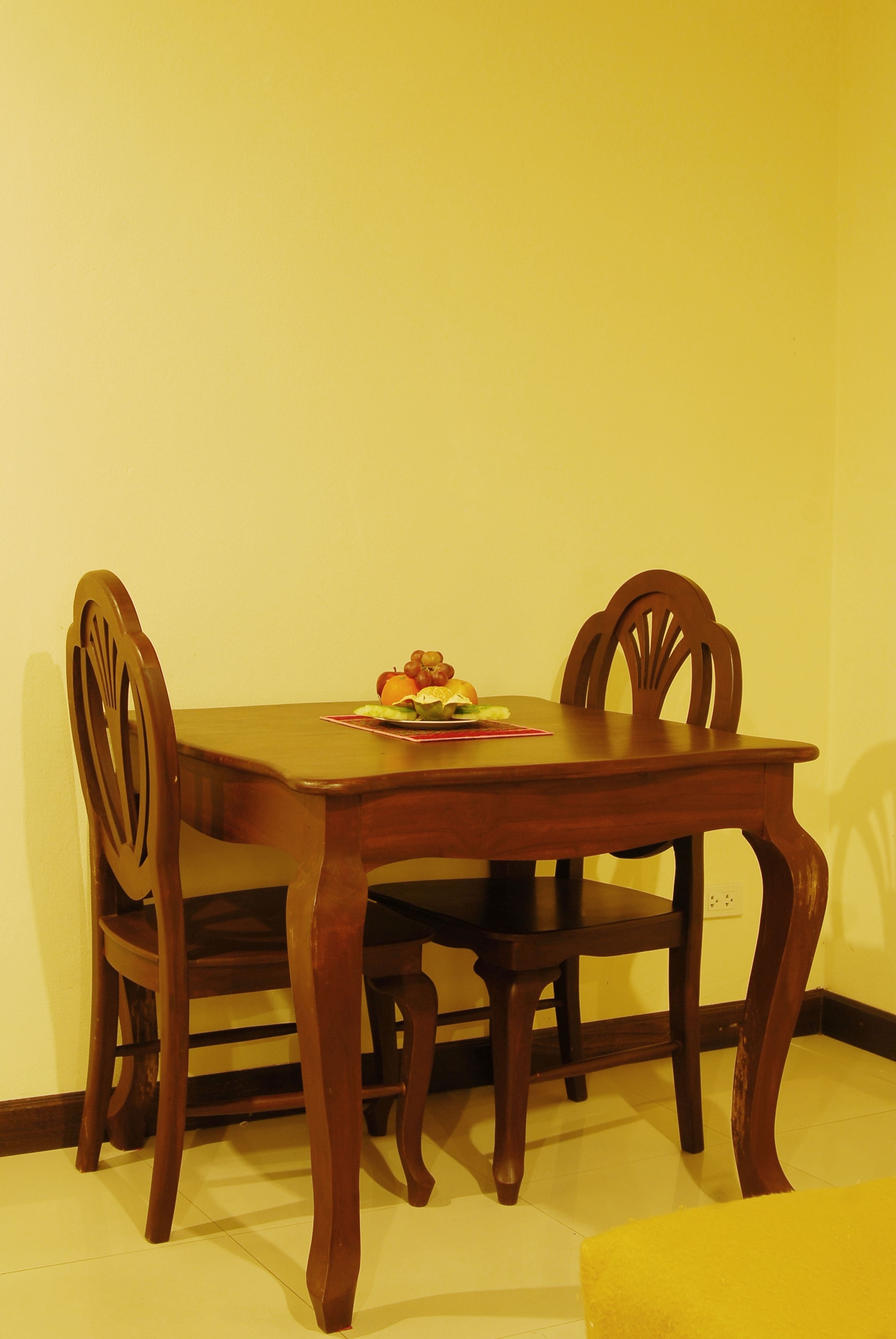 A wooden dining table with two chairs, a fruit bowl, and a small red placemat.