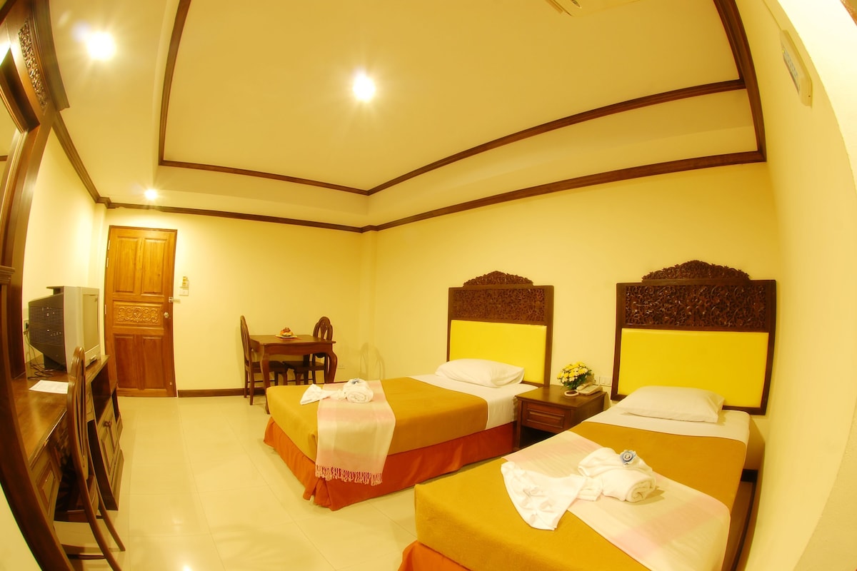 A hotel room with two beds, a desk, a chair, and a television.