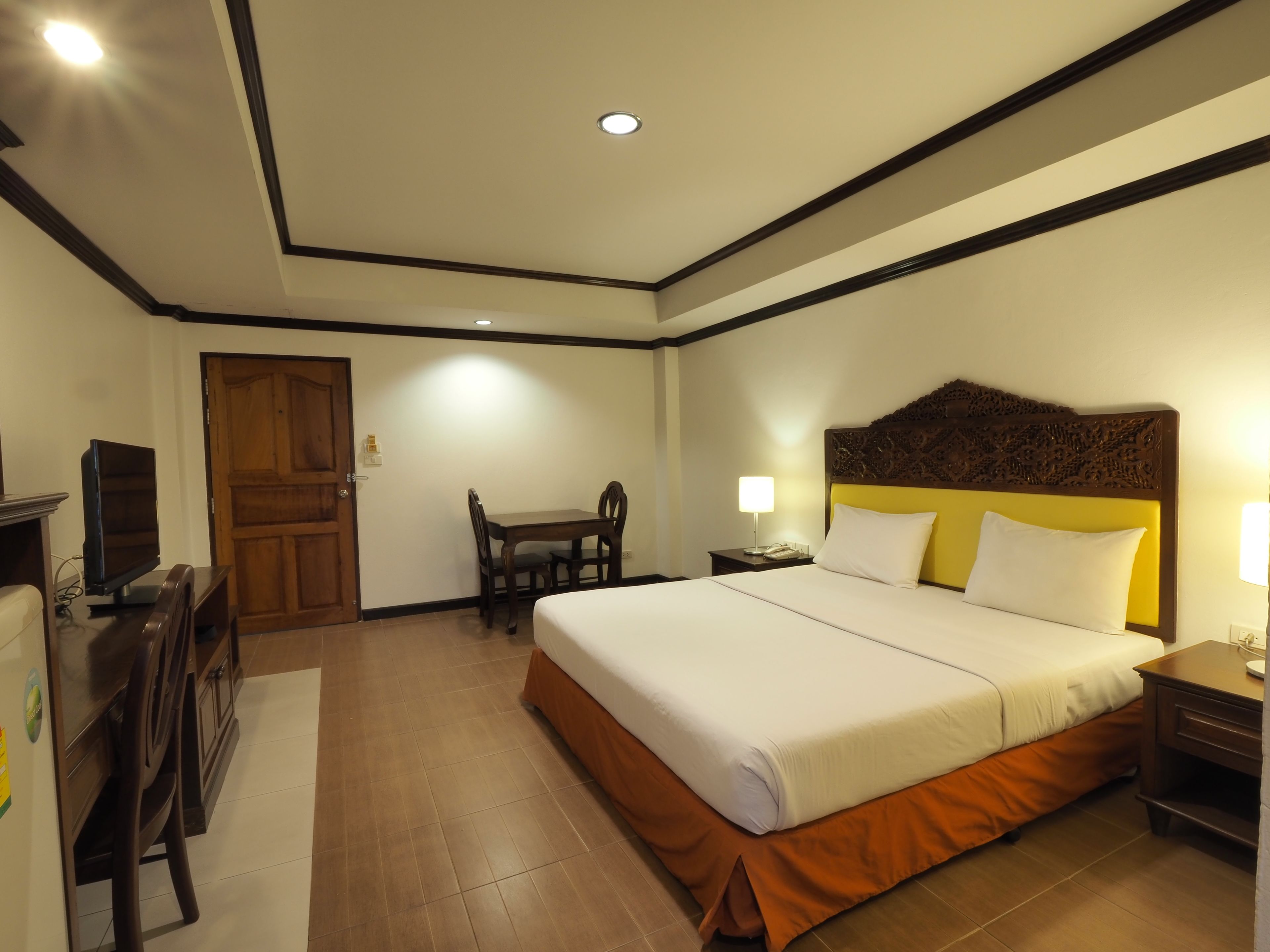 A hotel room with a bed, a desk with a chair, a television, and a door.