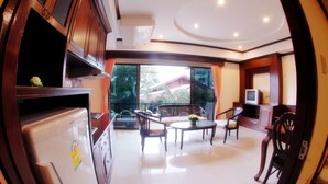 A spacious living area with a refrigerator, wooden cabinets, a television, and a balcony with outdoor furniture. - Golden Villa (Pattaya)