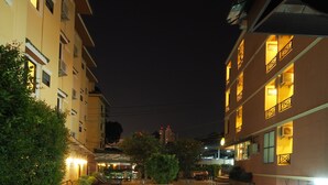 A nighttime swimming pool with tiled edges, surrounded by buildings with illuminated balconies and windows. - Golden Villa (Pattaya)