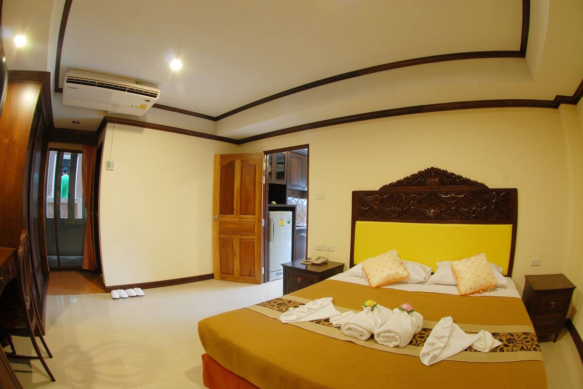 A hotel room with a bed, a nightstand, a wooden headboard, a wardrobe, and an air conditioning unit.