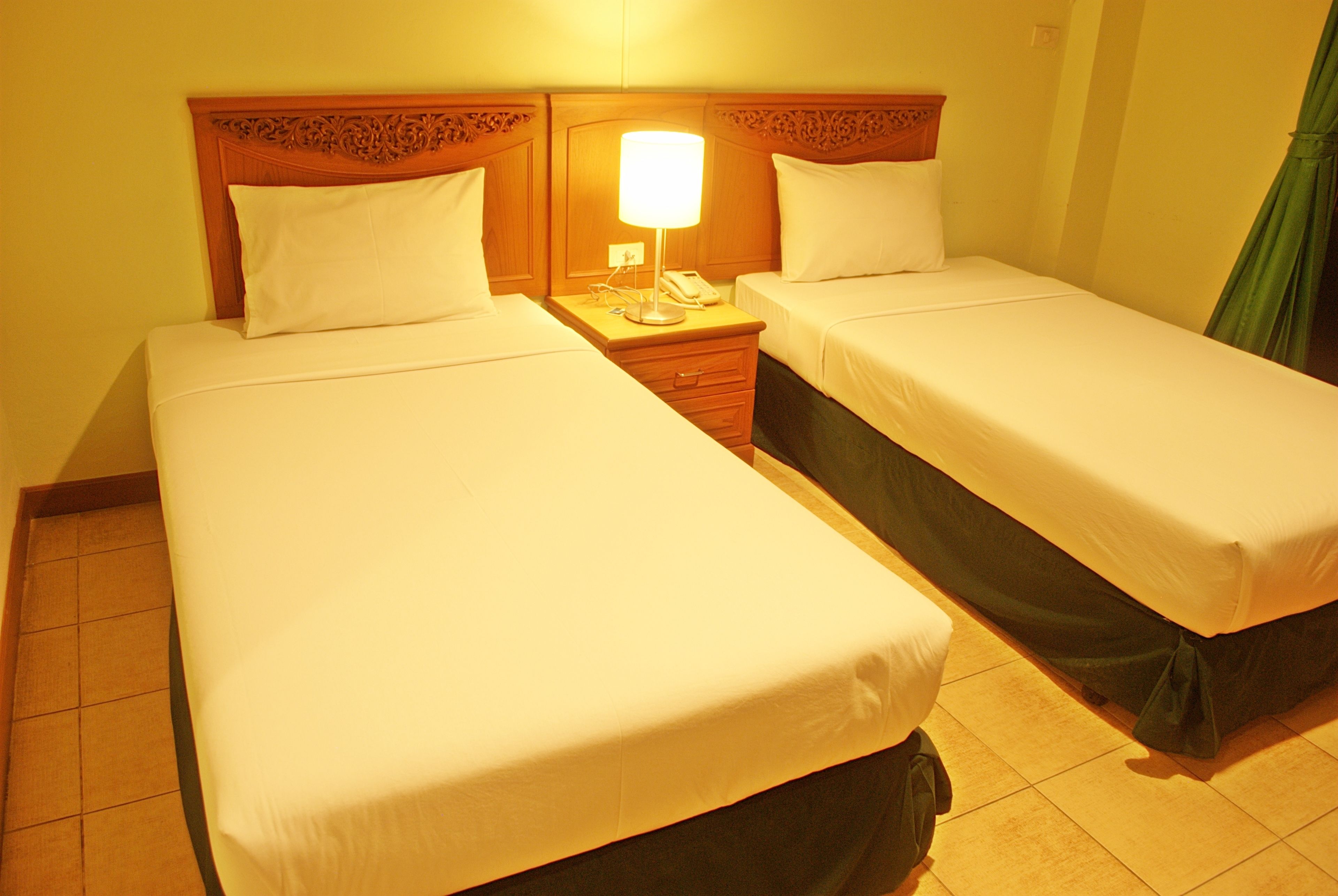 A hotel room with two single beds, a nightstand with a lamp, and a green curtain.