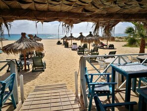 Une terrasse au bord de la plage, agrémentée de parasols en chaume et de chaises longues, d’où l’on peut admirer l’océan.