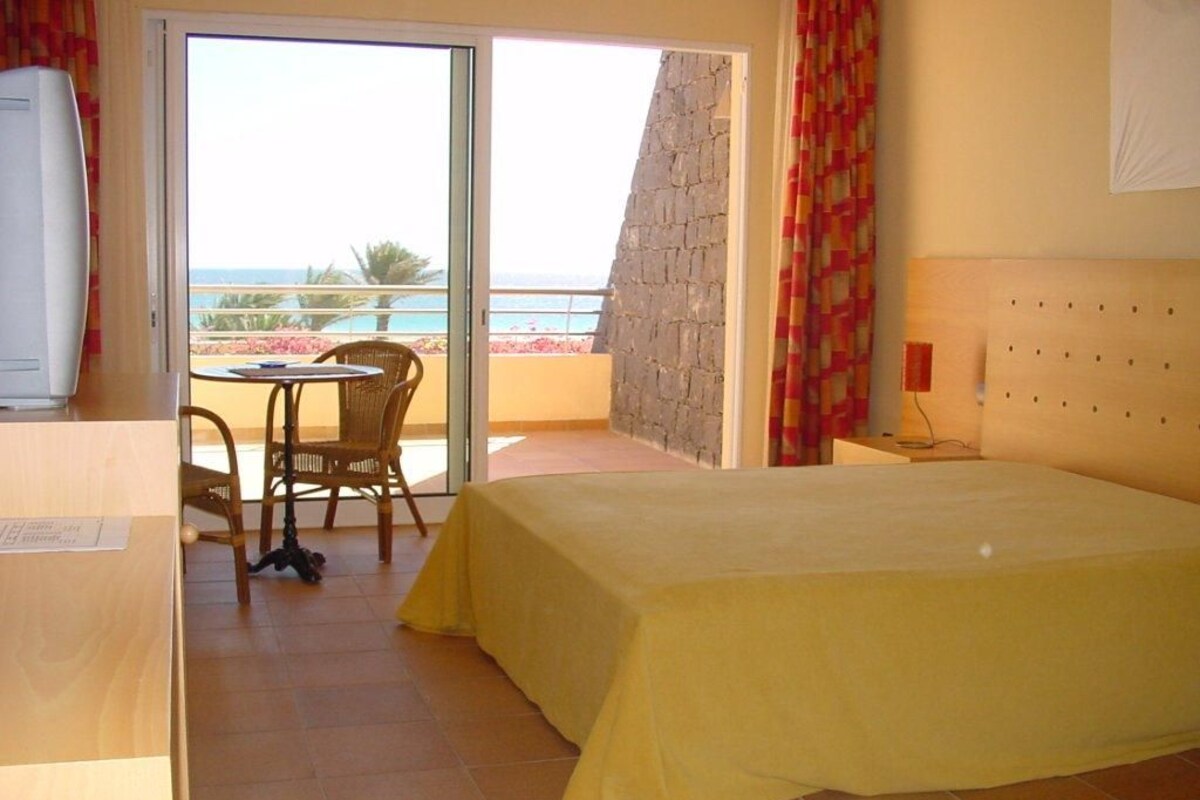 Habitación de hotel con cama, escritorio, silla y vista al océano.