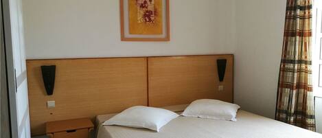Une chambre d’hôtel avec une tête de lit en bois, deux oreillers blancs, une petite table de chevet et une œuvre d’art encadrée accrochée au mur.