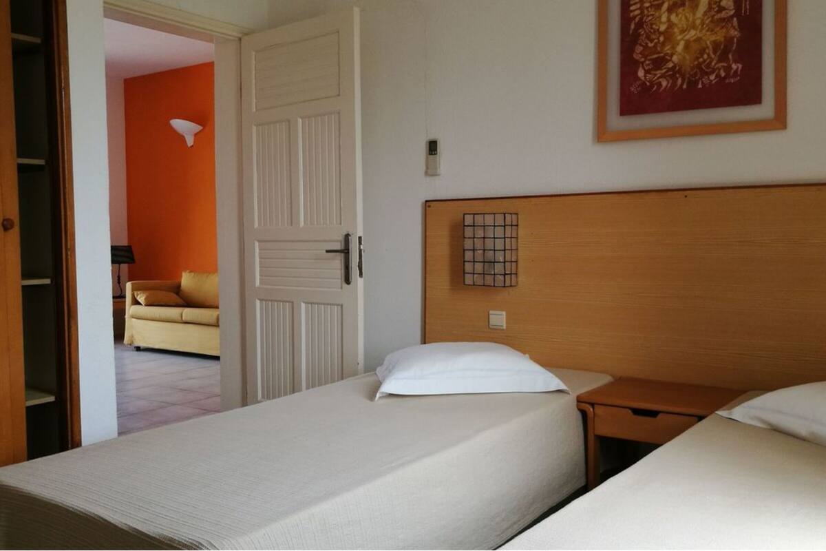 A hotel room with two single beds, a wooden headboard, a small bedside table, and a door leading to another room.