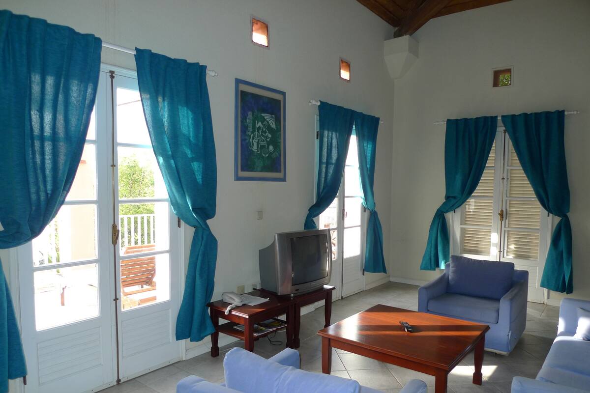 A living room with a TV, blue curtains, white sofas, and a wooden coffee table.