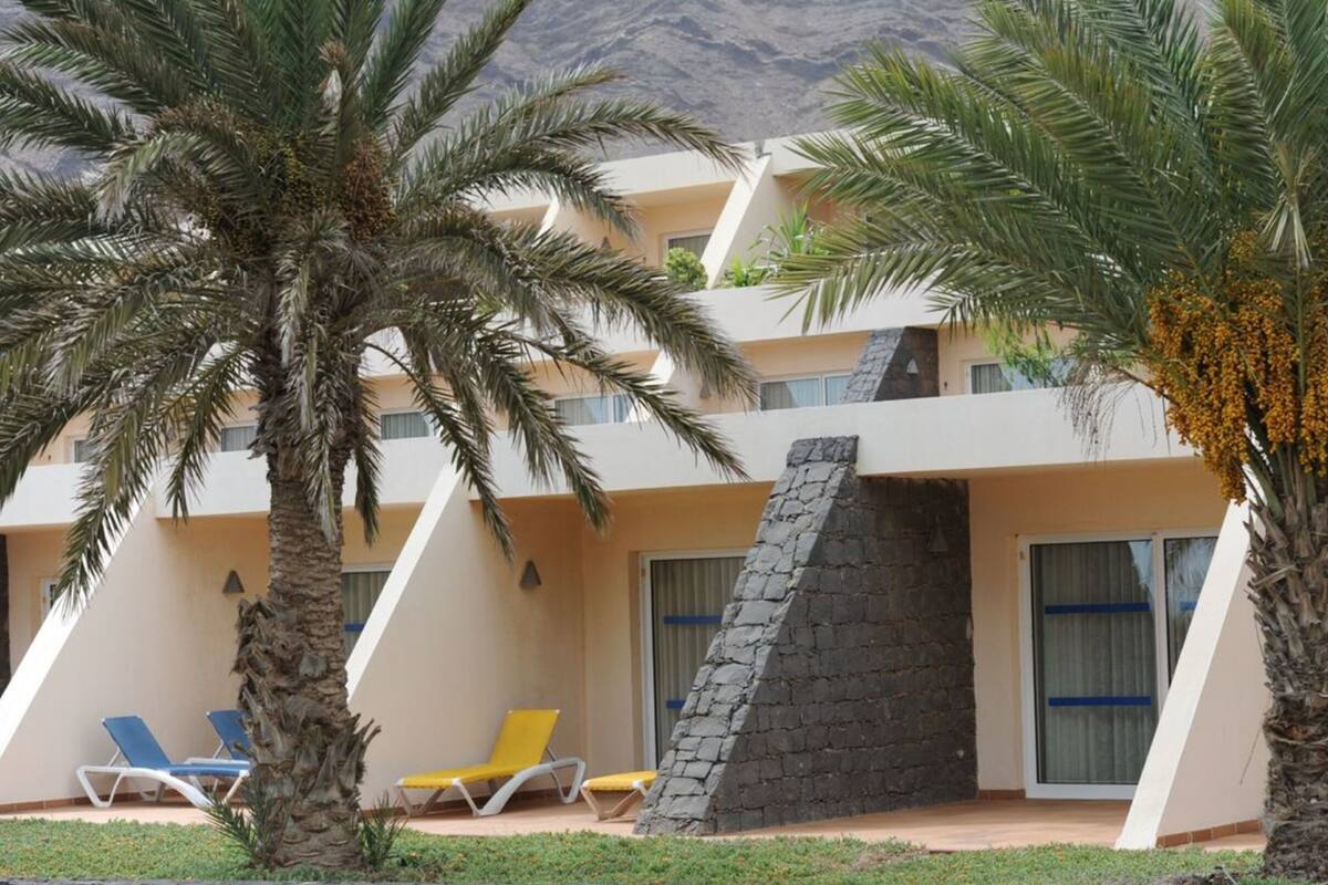 A hotel with a modern design, featuring a stone facade, multiple balconies, and palm trees.