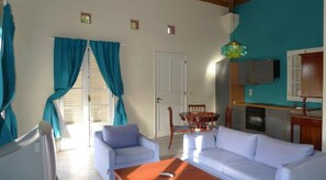 A living room with a sofa, a coffee table, and a dining area with chairs. There is a kitchen with cabinets and a sink. - Foya Branca by Flagworld Hotels (São Vicente)