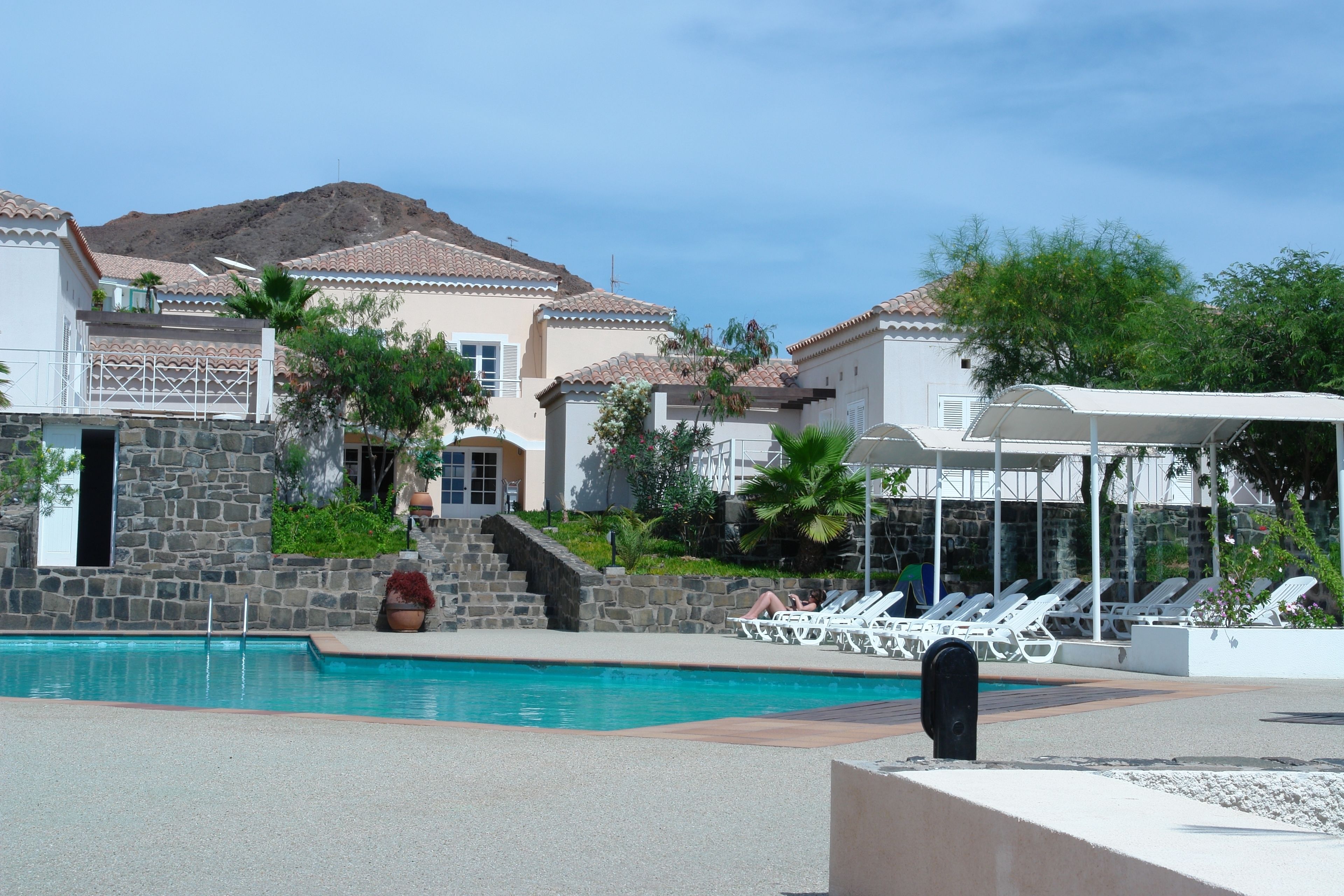 A pool area with lounge chairs, a stone wall, and a mountain in the background.