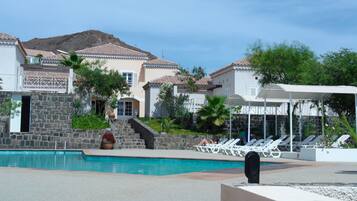A pool area with lounge chairs, a stone wall, and a mountain in the background.