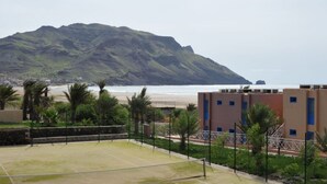 A tennis court with a net, surrounded by greenery and a building with blue windows. - Foya Branca by Flagworld Hotels (São Vicente)