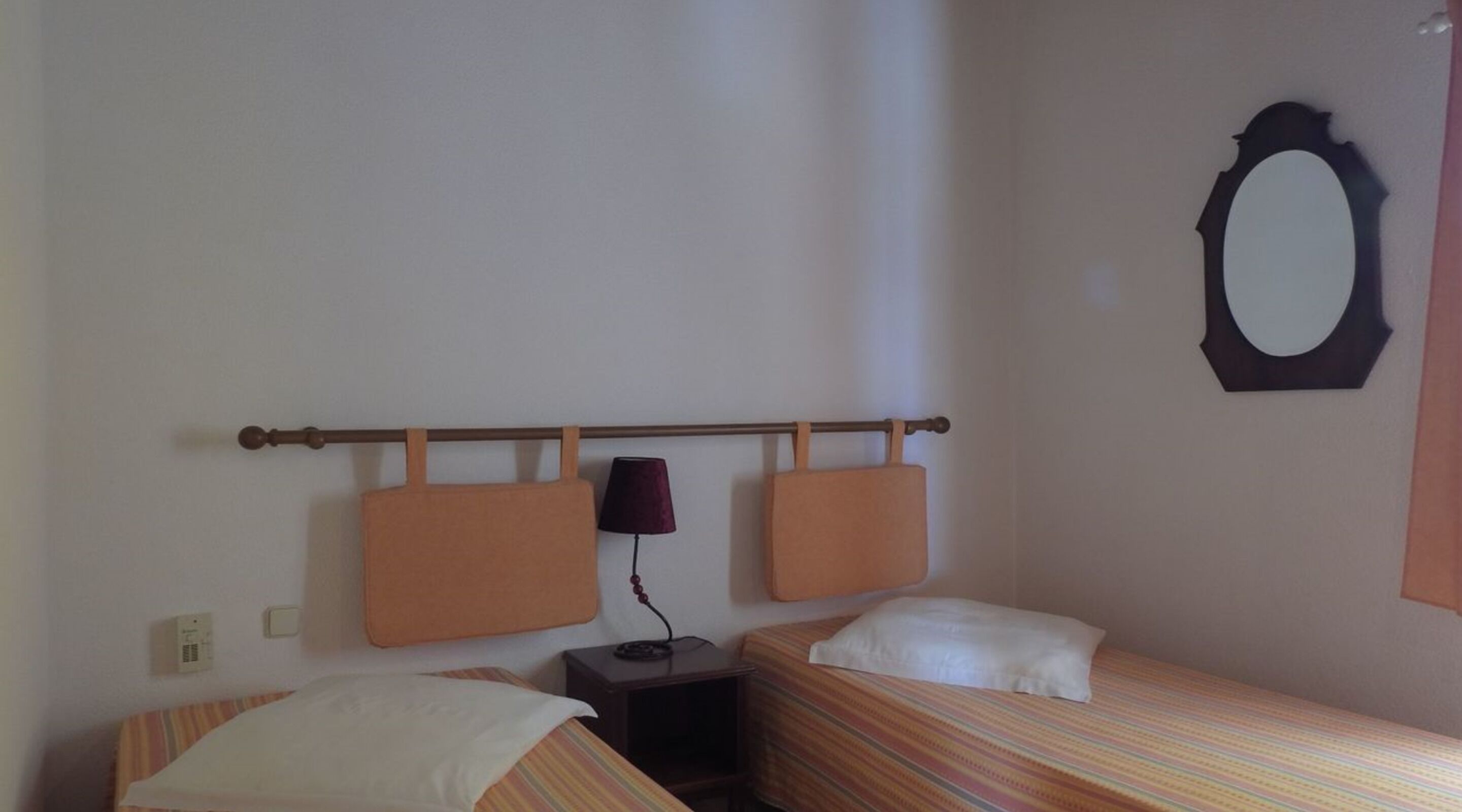 Een kleine, eenvoudige kamer met twee bedden, een nachtkastje, een lamp en een spiegel aan de muur.