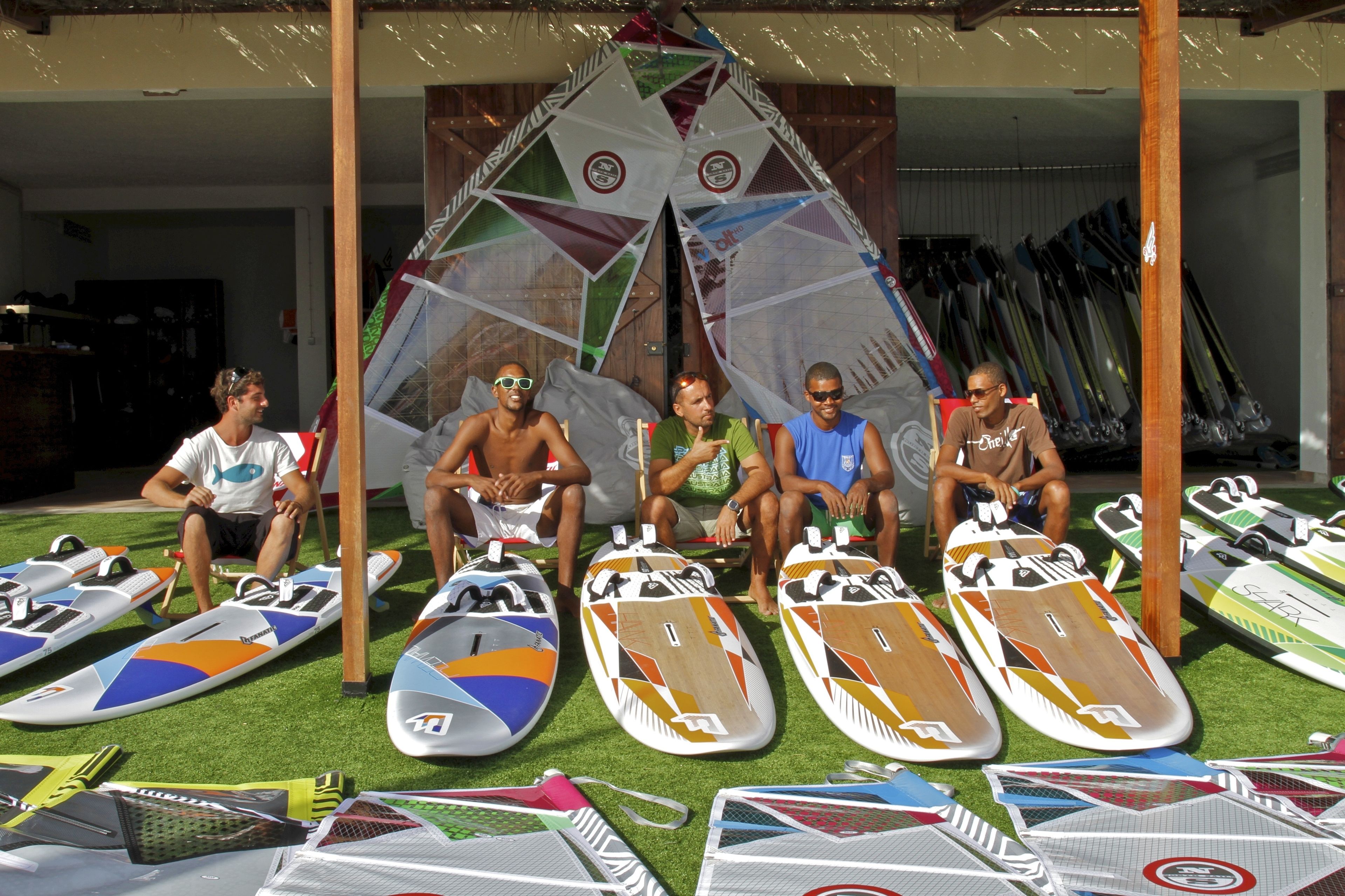 Un grupo de personas sentadas en sillas frente a tablas de surf y una cometa grande.