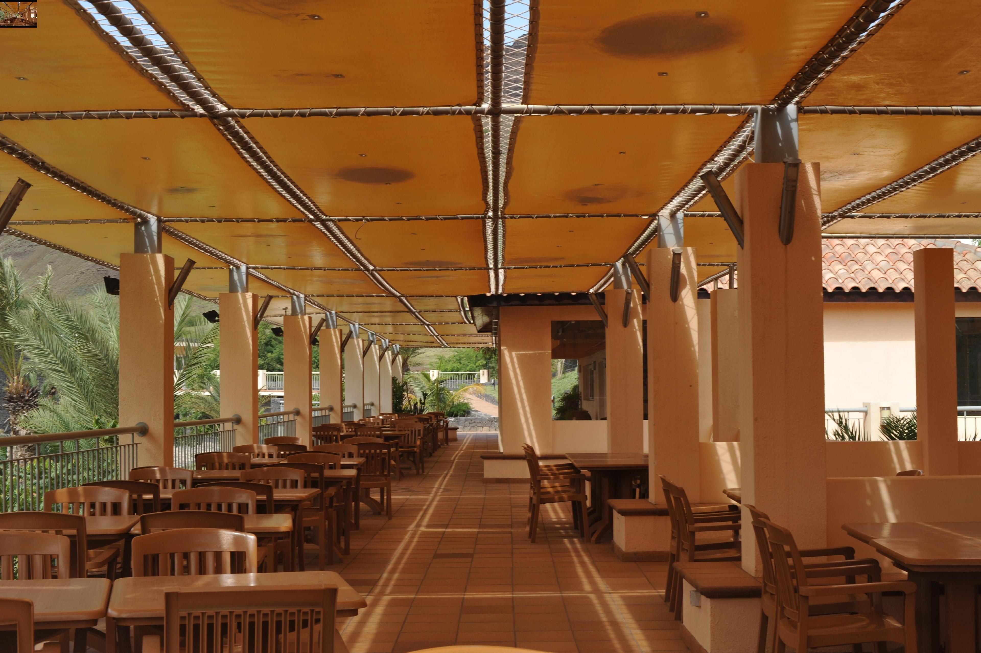 An indoor dining area with wooden tables and chairs, a tiled floor, and a ceiling with a patterned design.