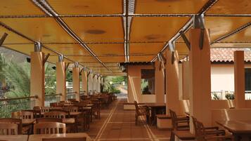 An indoor dining area with wooden tables and chairs, a tiled floor, and a ceiling with a patterned design.