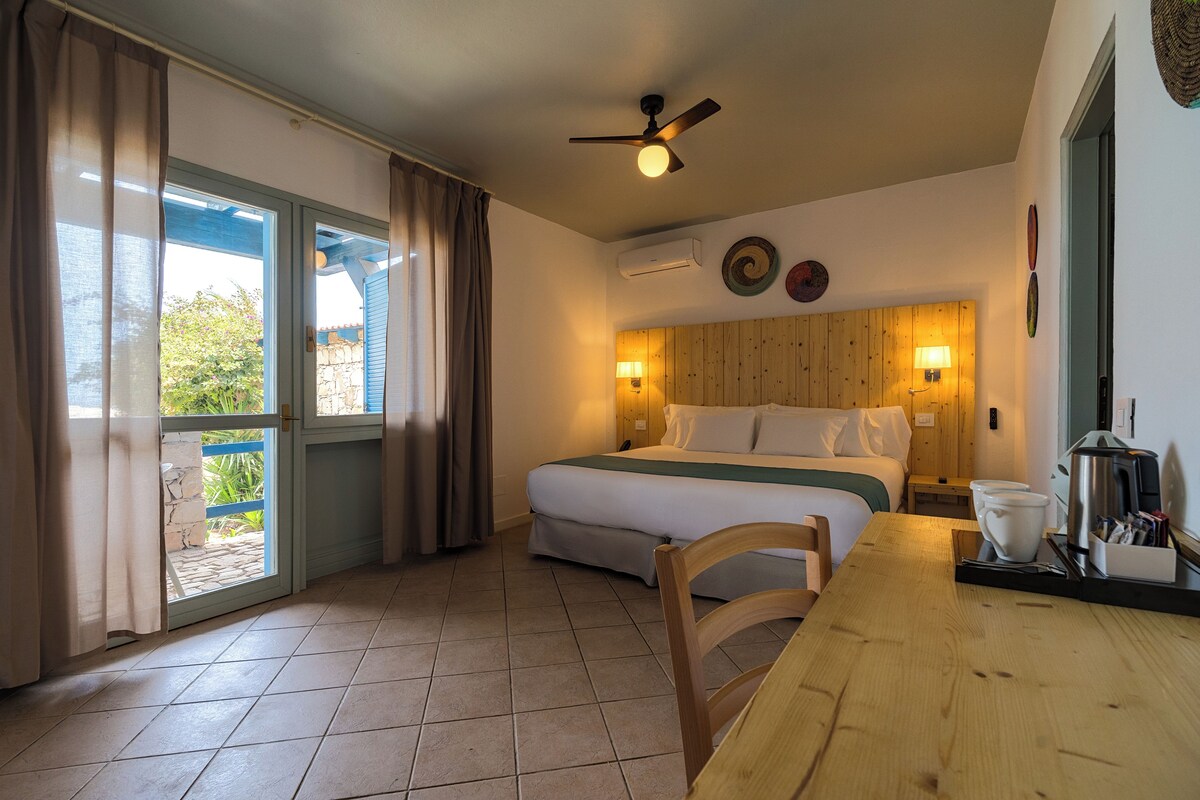 Een hotelkamer met een bed, een bureau, een stoel, een plafondventilator en een raam met gordijnen.