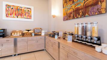 A breakfast buffet area with various food options, a coffee machine, and artwork on the walls.