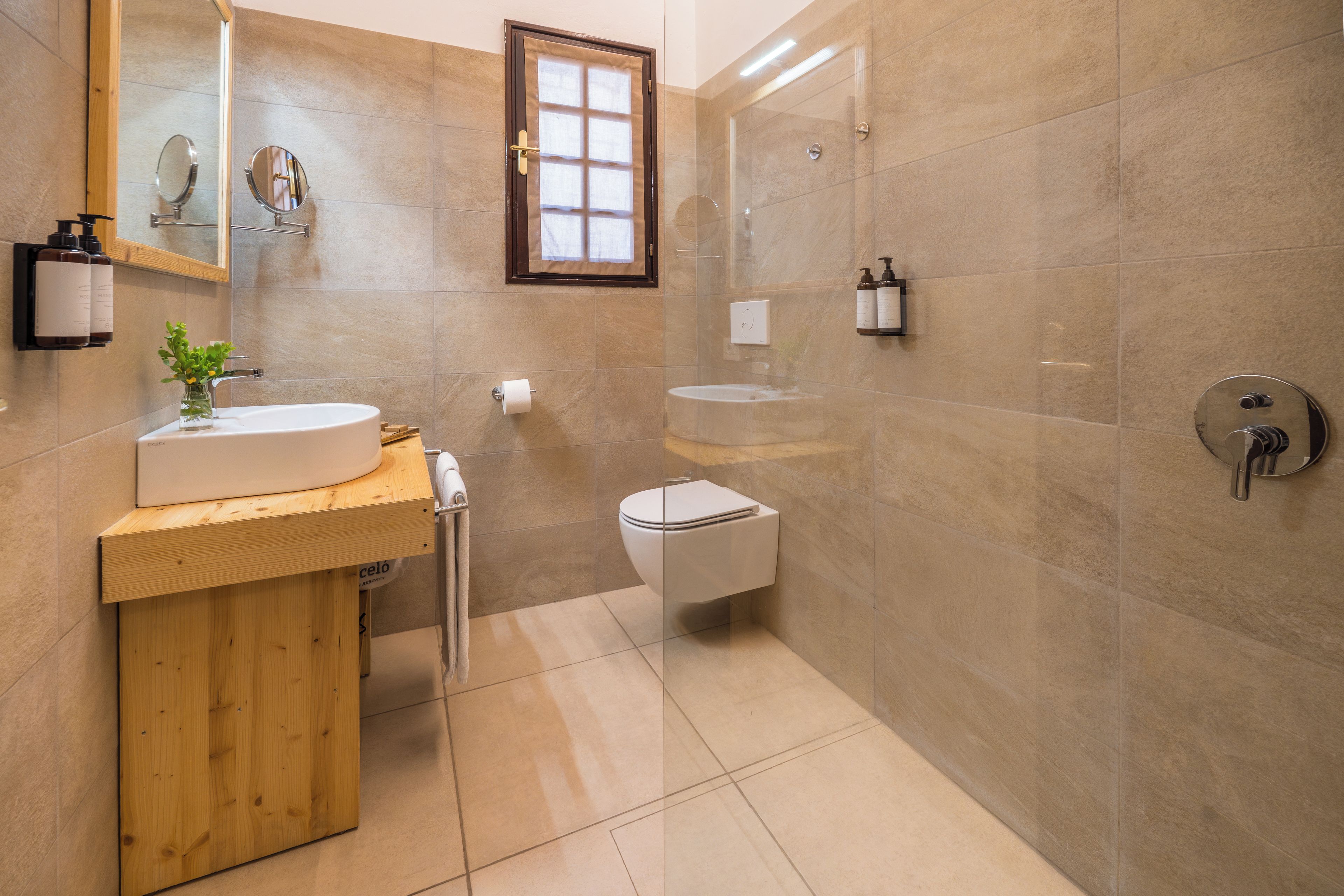 A modern bathroom with a wooden vanity, a round mirror, a toilet, and a shower area.