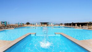 Une piscine agrémentée d’une fontaine centrale, entourée de chaises longues et de parasols.