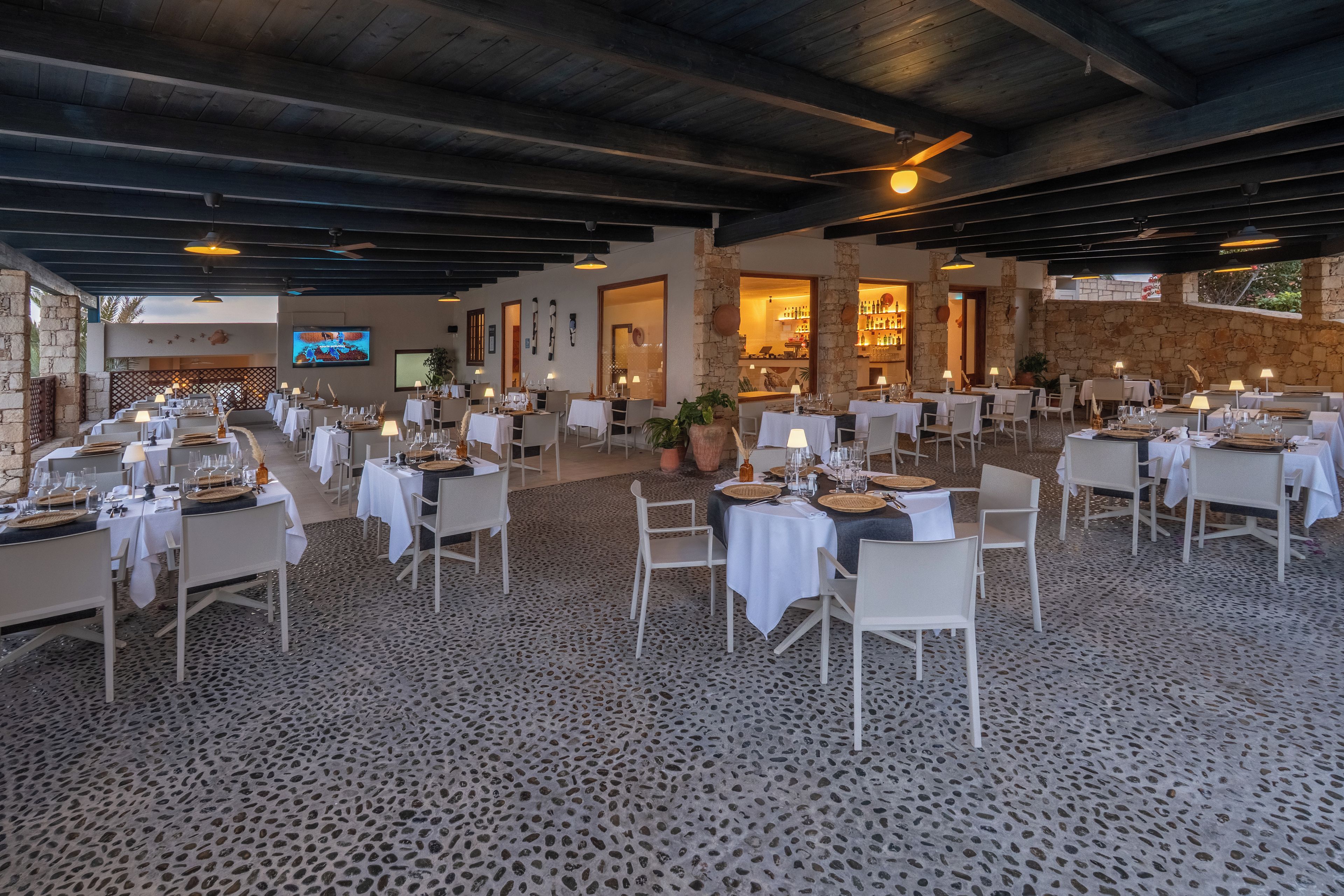 A restaurant with multiple tables set for dining, stone walls, and a television screen.