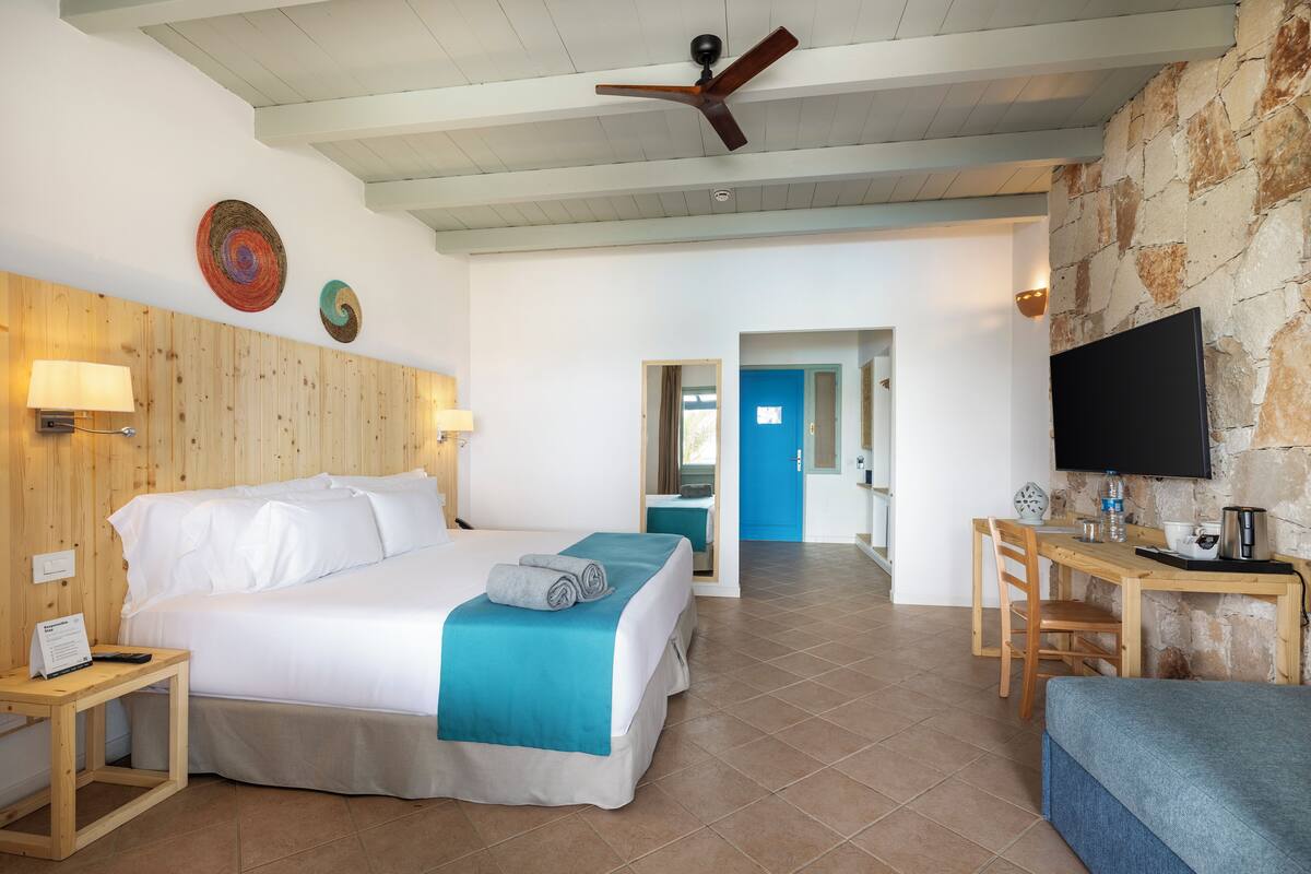 Habitación de hotel con cama, escritorio, televisión y baño visible a través de una puerta abierta.