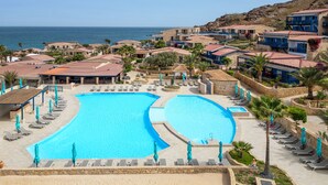 Un resort con una gran piscina, varias zonas de descanso y vistas al mar.