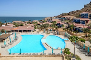 Een resort met een groot zwembad, diverse loungegedeeltes en uitzicht op zee.