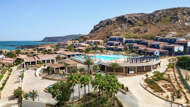 Un resort con piscina central, palmeras y vista al mar.